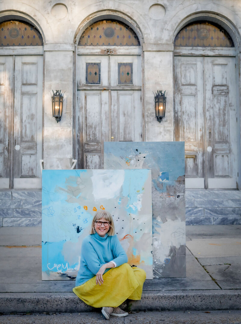 Adele sitting on curb in front of two abstract paintings