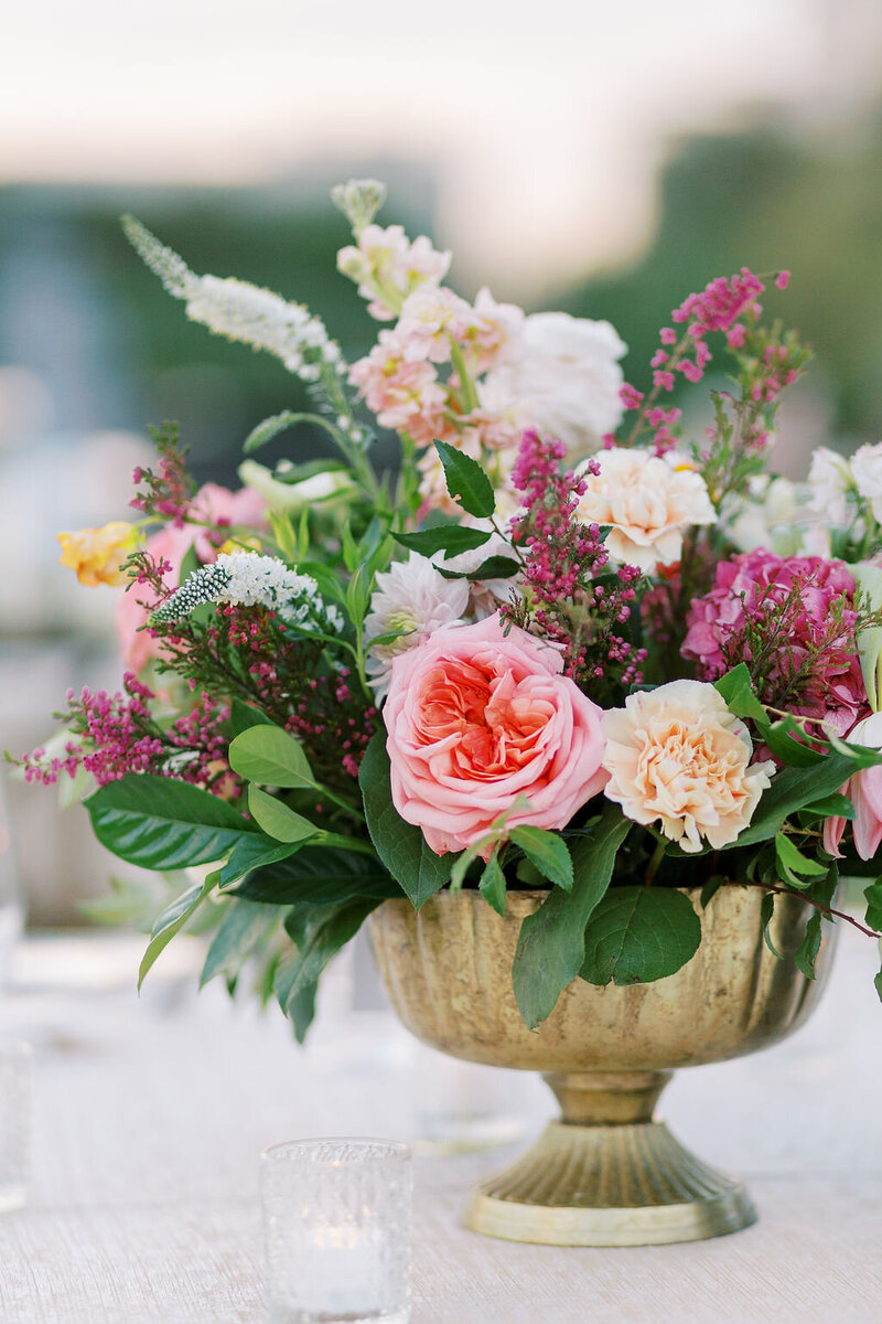 Close up of a pink and white floral arrangement with greenery in a gold vase