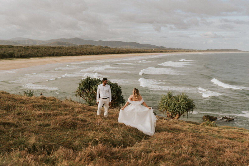 A Sawtell wedding photoshoot of a bride running across a headland field to her groom overlooking the beach
