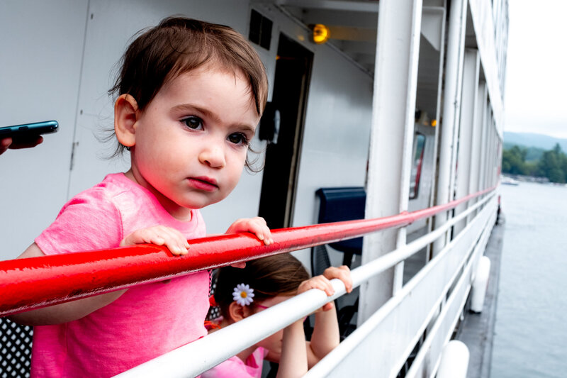 A little girl is looking out the railing of a boat.