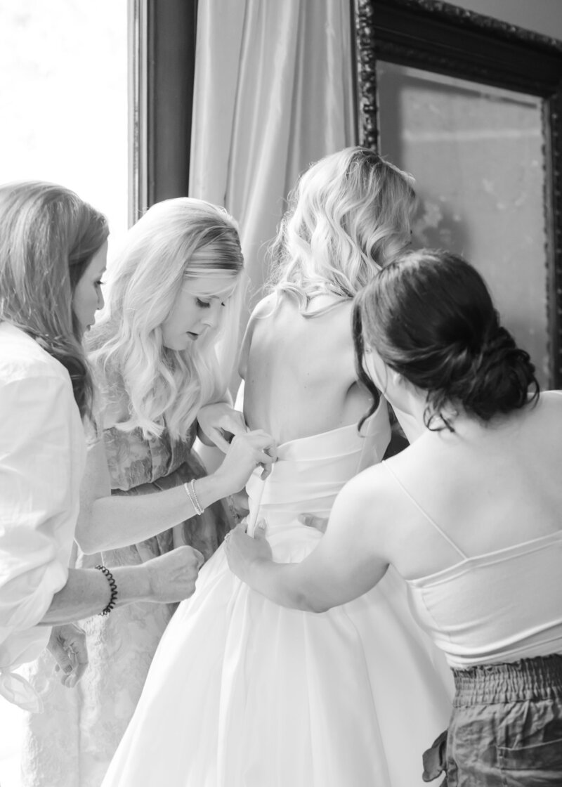 Lucy's mom and friends button her wedding dress at Blackstone Rivers Ranch wedding venue.