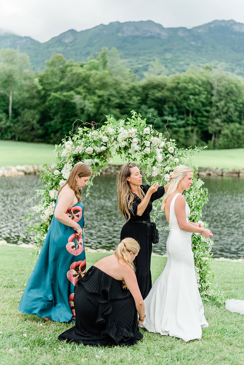 Wedding planner and bridesmaids fix bride's hair and dress