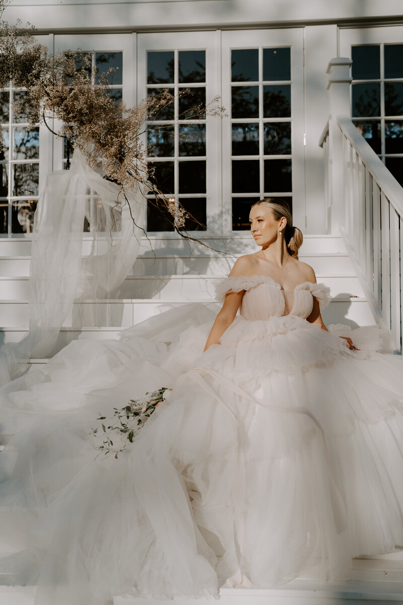 Kwila Lodge steps with a bride sitting in a fluffy full gown with a bridal ponytail and peach makeup