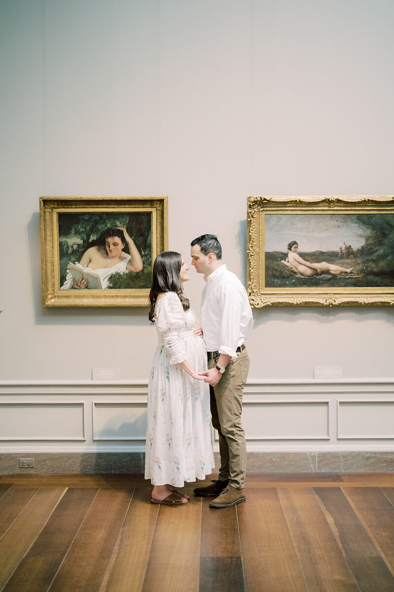 Pregnant couple stand facing one another in the National Gallery of Art.