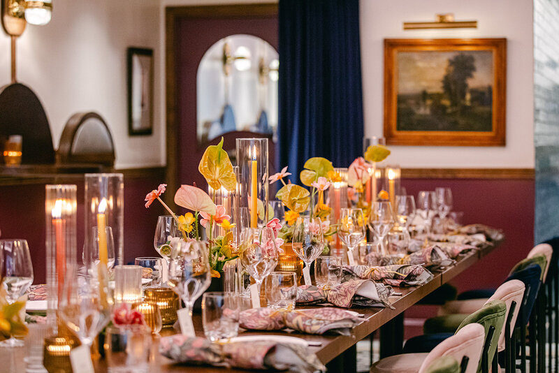 A beautifully set long-table rehearsal dinner at L'Artusi Supper Club in New York City, featuring warm candlelight, floral centerpieces, and an intimate atmosphere.