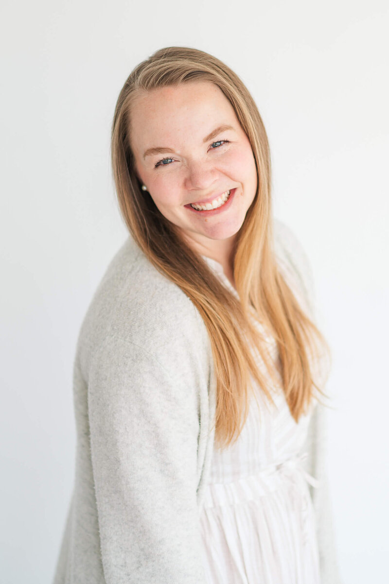 Headshot of a blonde woman in light clothing smiling at the camera.