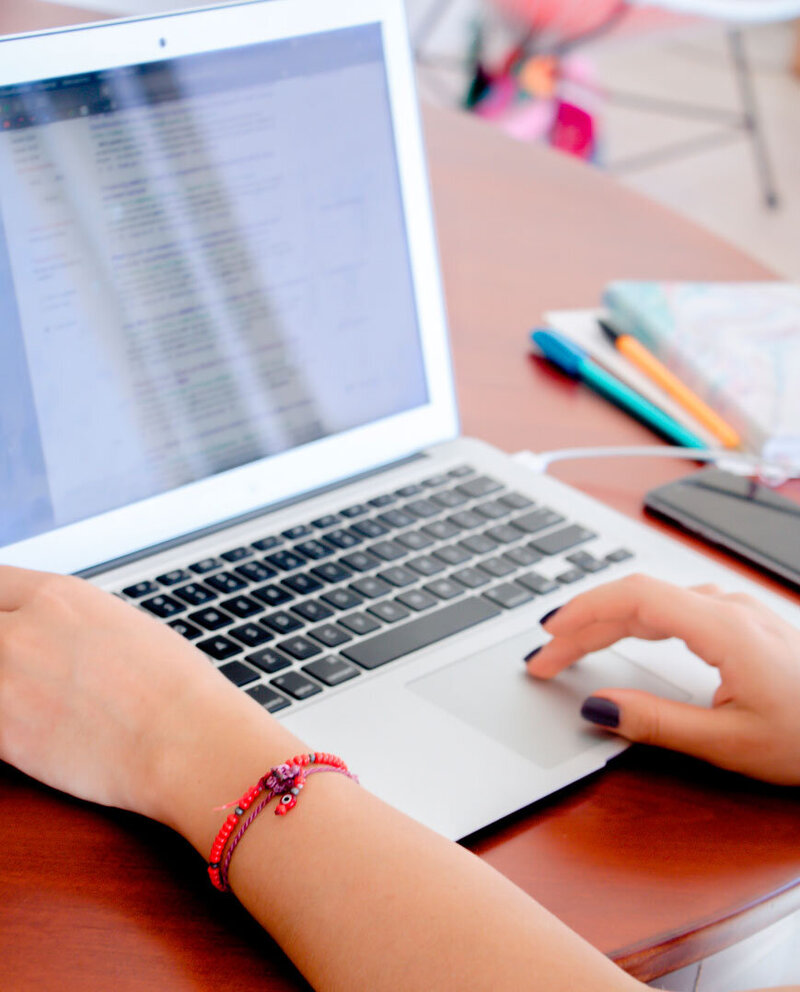 PPC marketer working on a digital marketing project using a laptop. The office desk features color pens and an agenda, emphasizing organization and creativity.