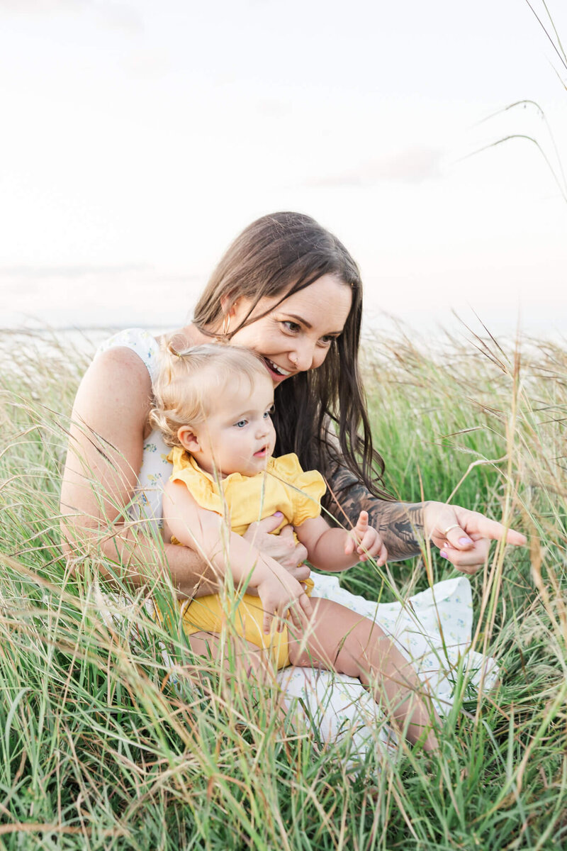 A sweet moment being shared between a mum and her toddler daughter while seated in green grass on top of a Cooee Bay hill near Yeppoon.