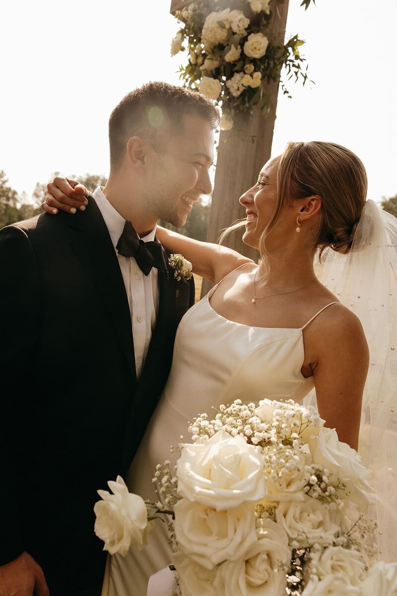 Couple on their wedding day looking at each other smiling with a white bouquet