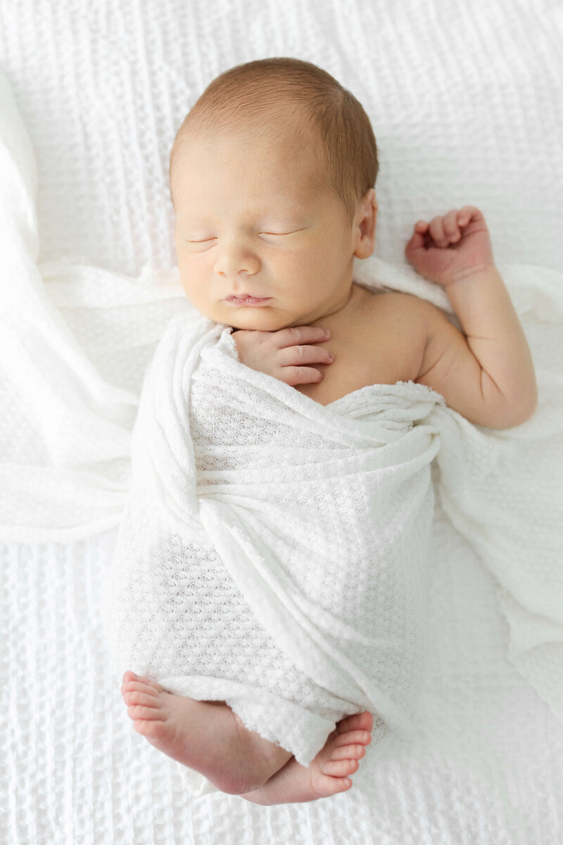 Newborn baby wrapped in white baby wrap sleeping during newborn photography session in Dothan Alabama Photography Studio
