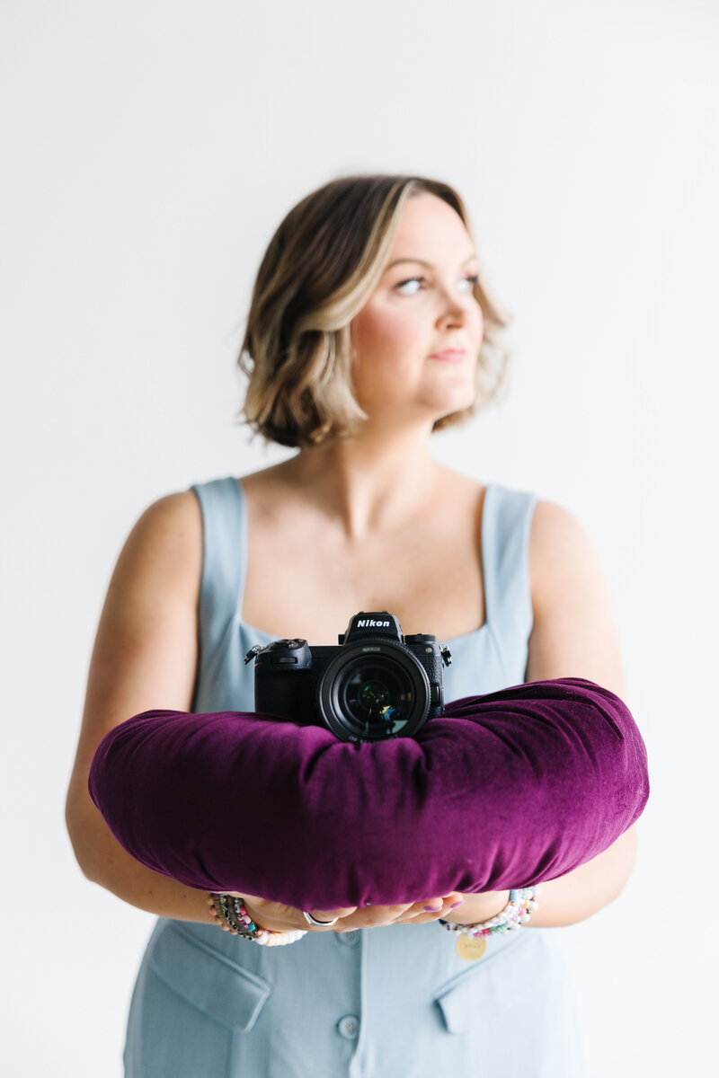Woman in blue jump suit holding a purple pillow with a camera placed on it