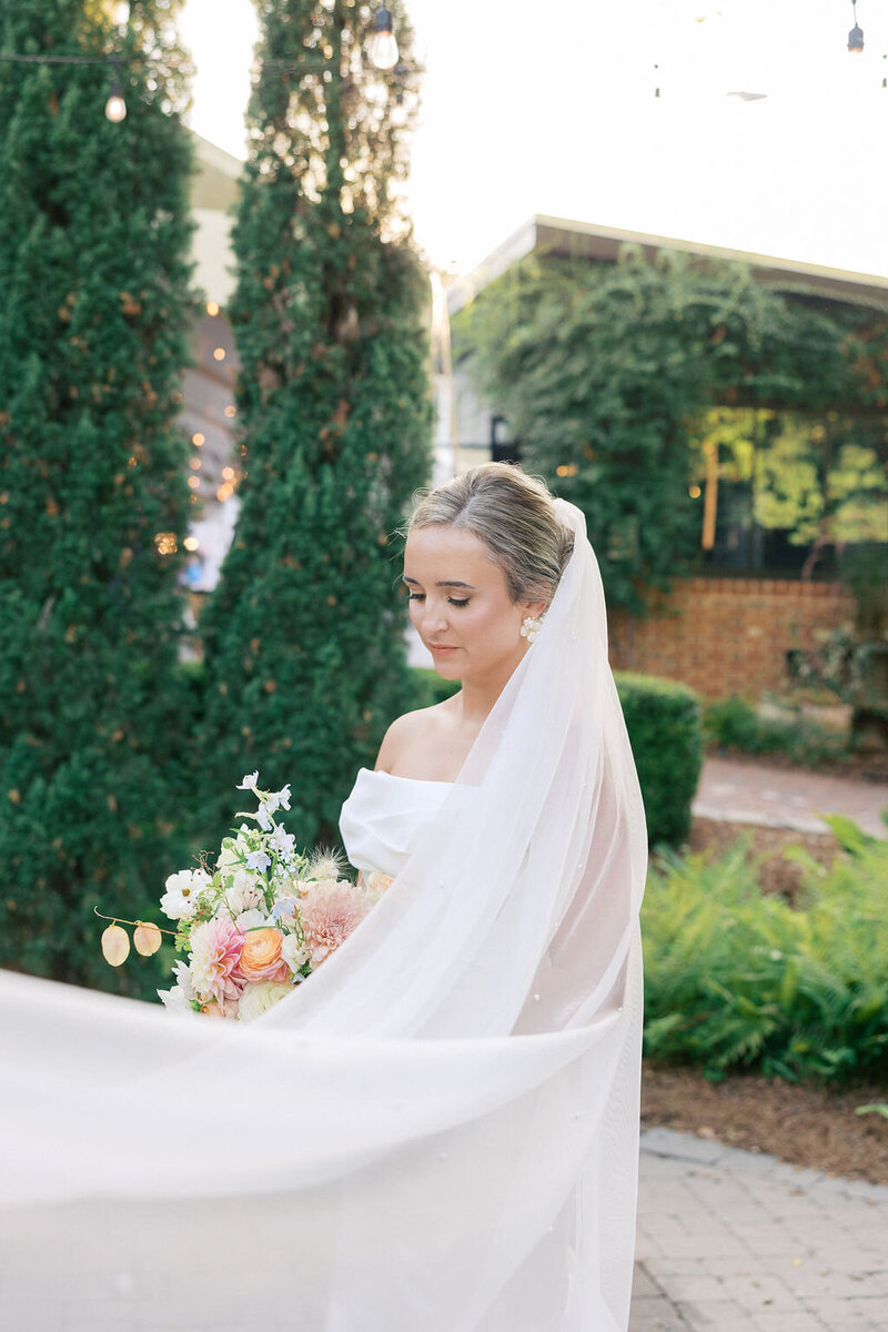 Bride holds pastel bouquet and looks softly at greenery at 255 Milledge