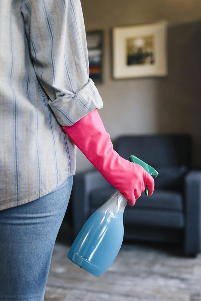Woman wearing a pink cleaning glove and holding a bottle of cleaning liquid