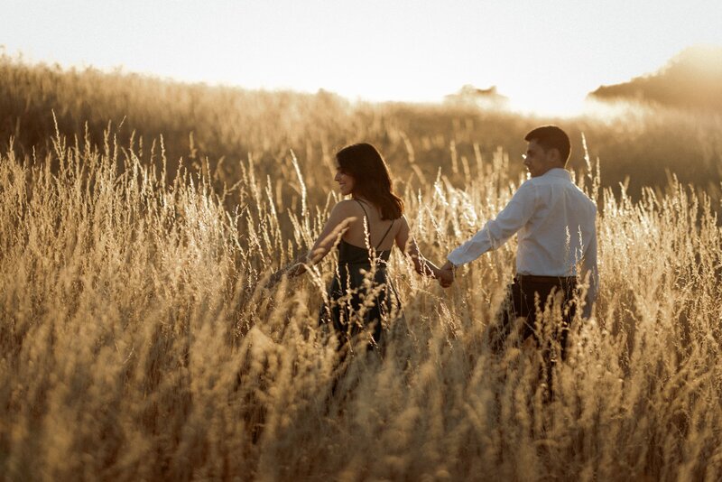 A romantic couple holding hands on  walking in the grass in beautiful golden hours in sunset