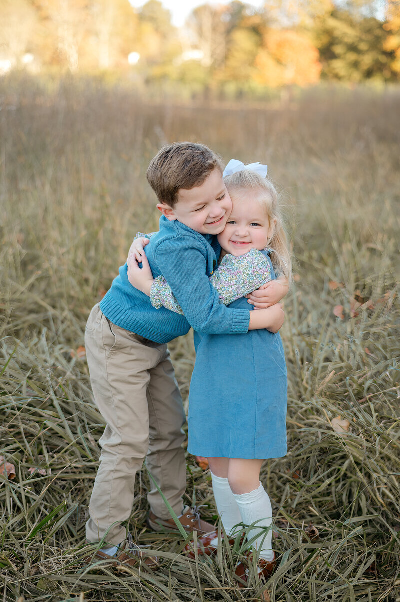 Young siblings hug one another and smile in the field at Prospect Farms. Photo by Atlanta family photographer Amanda Touchstone