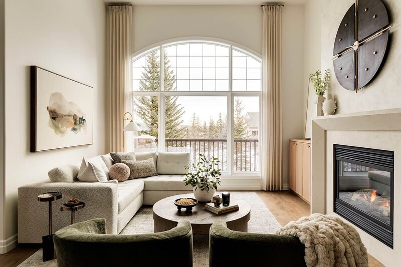 Custom living room sectional with abstract neutral artwork and round wooden coffee table with hints of green and stationary custom drapery panels.