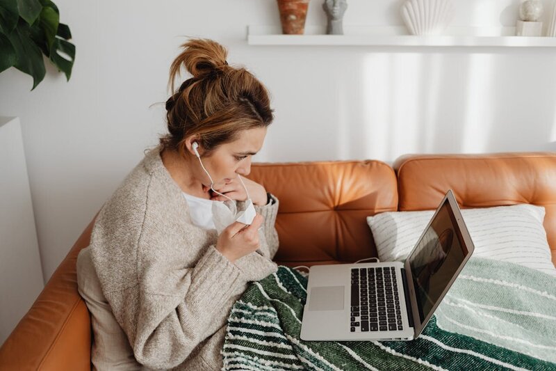 Woman sitting on a couch with a laptop and headphones representing a calm virtual therapy setting beside text outlining payment policies and flexible options at Rooted & Nourished Psychotherapy