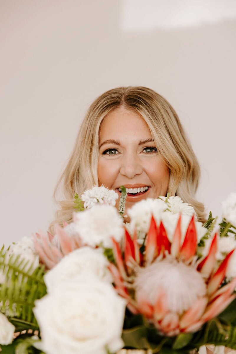 Portrait of Dana, DWD’s founder, smiling behind a vibrant bouquet of tropical and blush flowers.