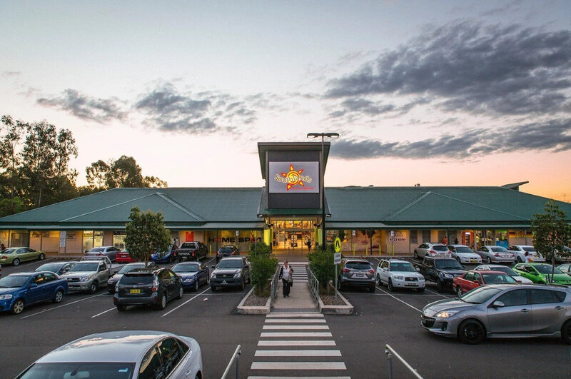 Southlands Shopping Centre in South Penrith, NSW, developed by Serlana Constructions — evening shot highlighting the welcoming retail entrance, signage, and full parking lot serving the residential community.