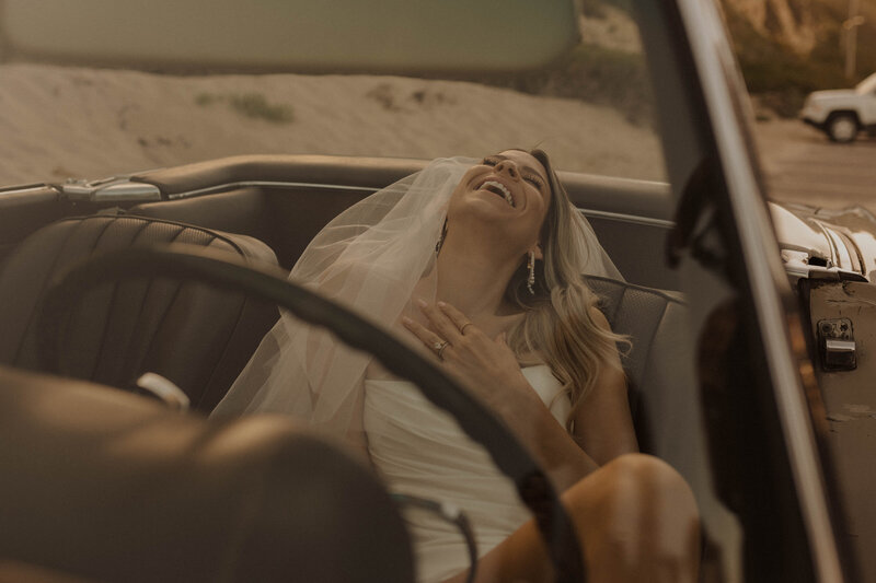 elopement bride laughing in the drivers seat of a classic car