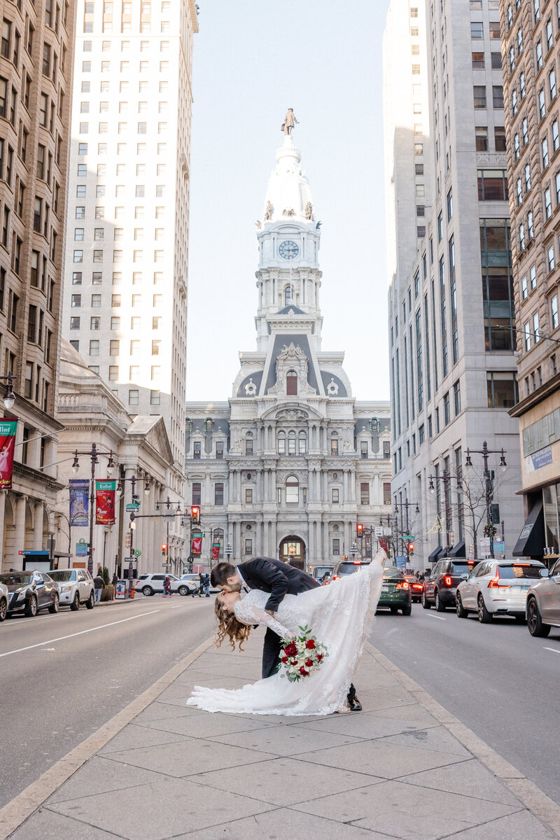 A bride and groom dip kisses in Philadelphia with City Hall visible behind them. Photo by Christopher Ginn Studios.