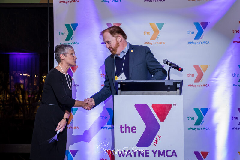 The man is shaking hand with the woman on the stage a YMCA fundraising gala.