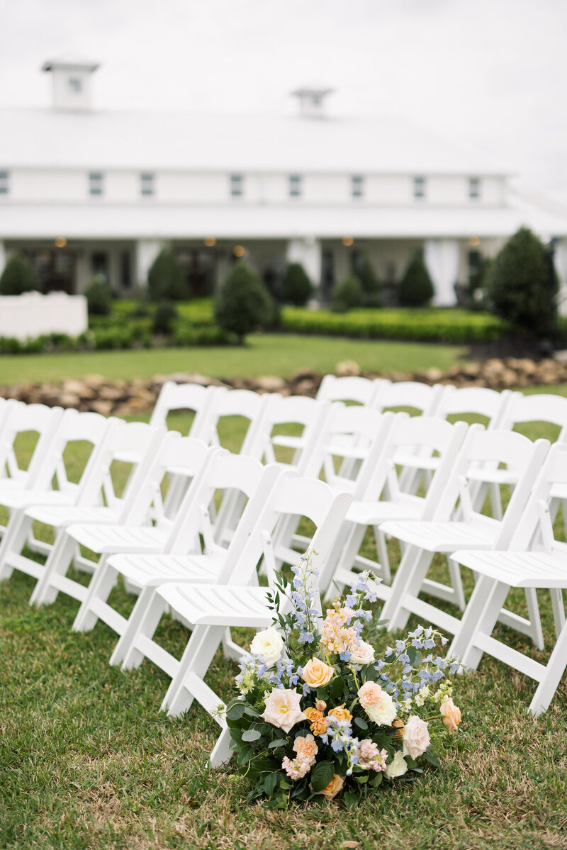 Wedding ceremony setup with white chairs and vibrant blue, pink, and orange flowers, captured by Morgan Alysse, Louisiana wedding photographer.