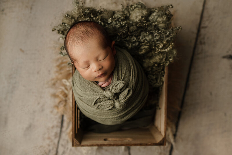 newborn baby boy in green in crate