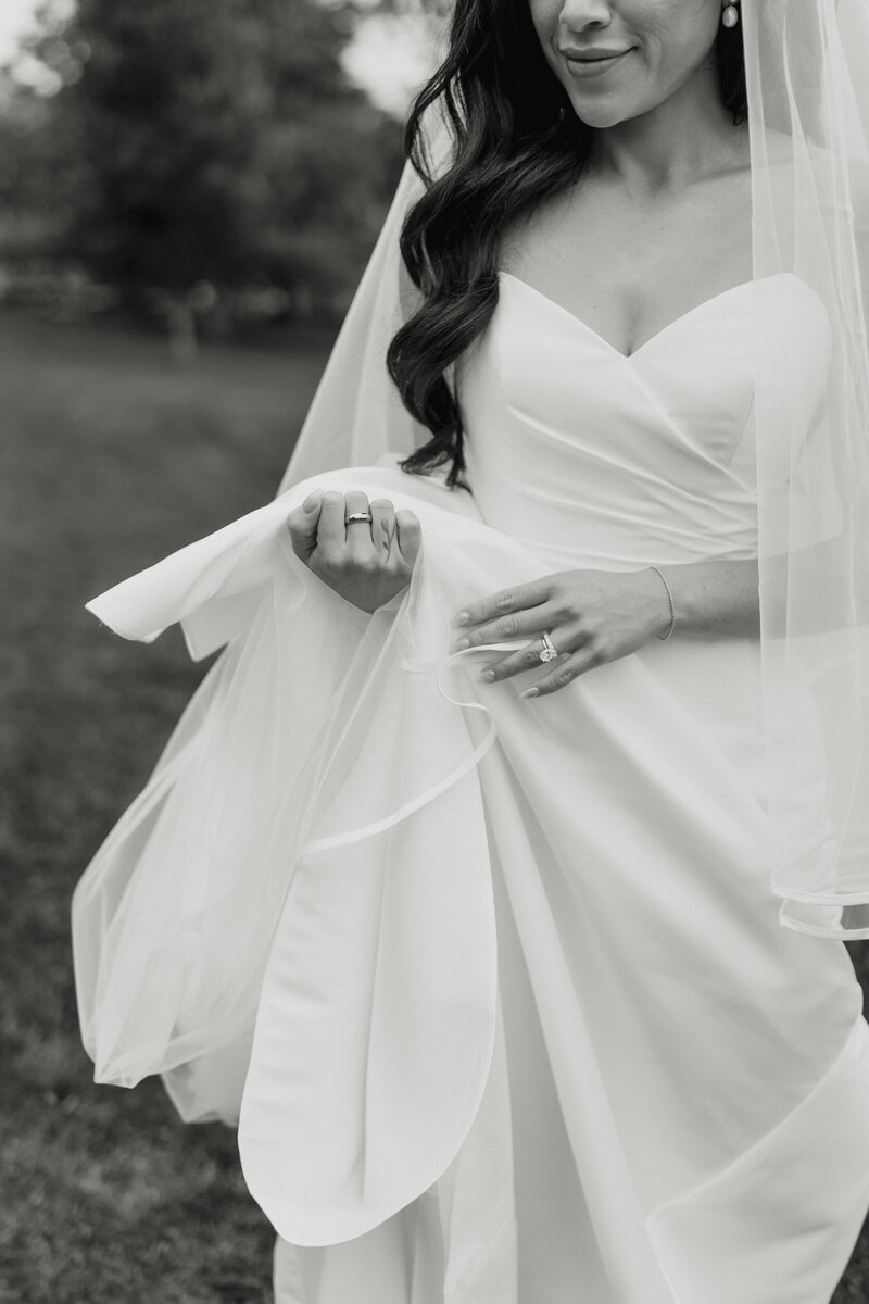 A black and white detail photo of a bride holding up her dress.