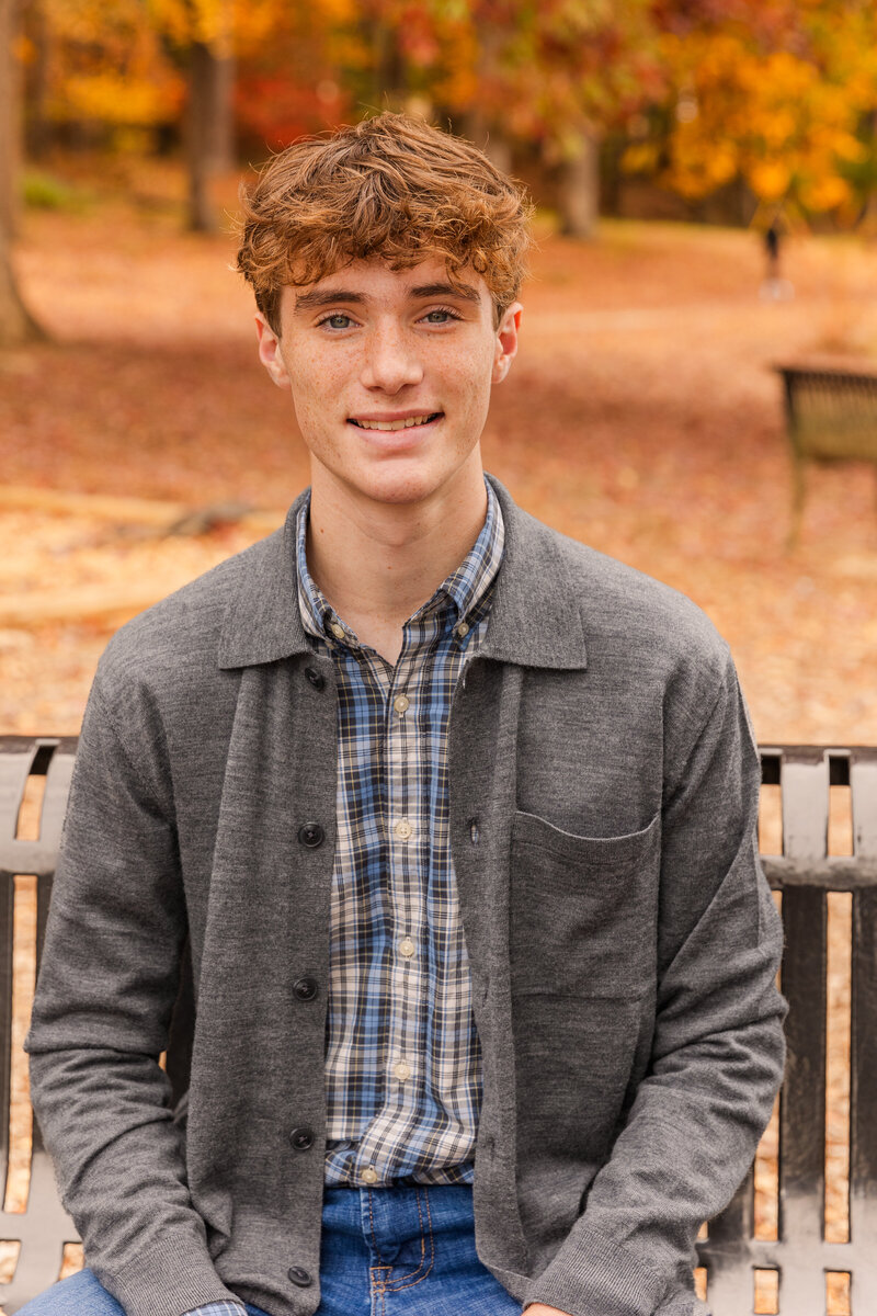 High school senior boy sitting on a bench in a park during photoshoot by photographer Laure Photography