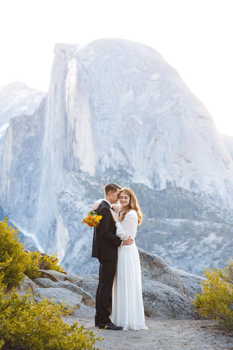 bride and groom embrace in front of Half Dome in Yosemite National Park