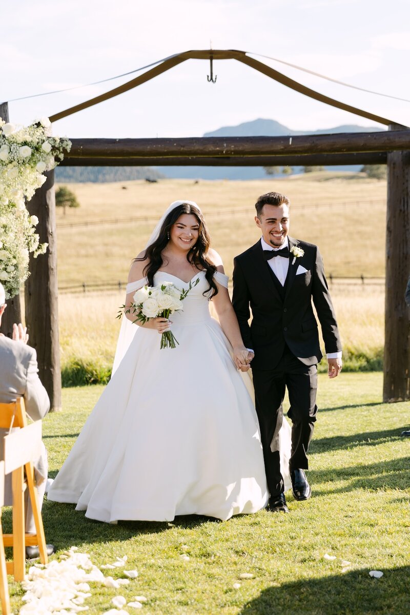 Bride and groom leaving their wedding ceremony at Spruce Mountain Ranch—a luxury Colorado wedding venue with mountain views.
