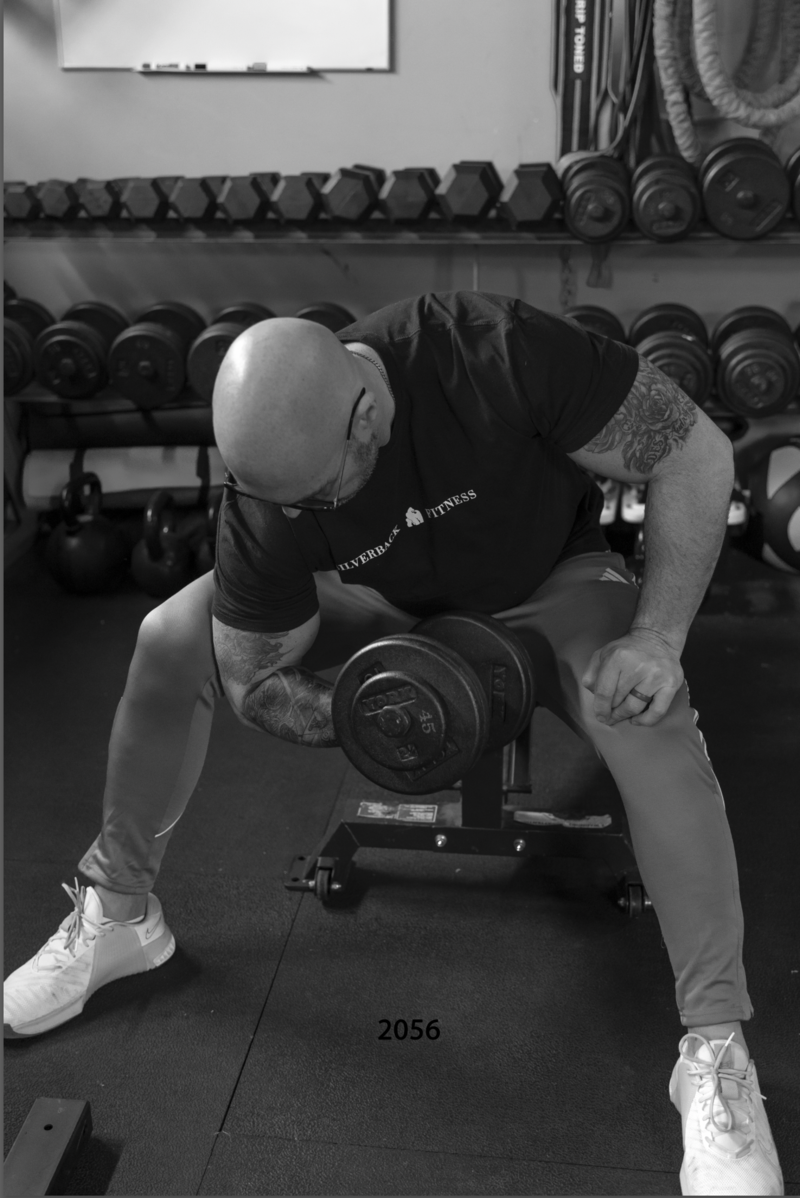 Man is doing bicep curls at his home gym under instruction from his online personal trainer.