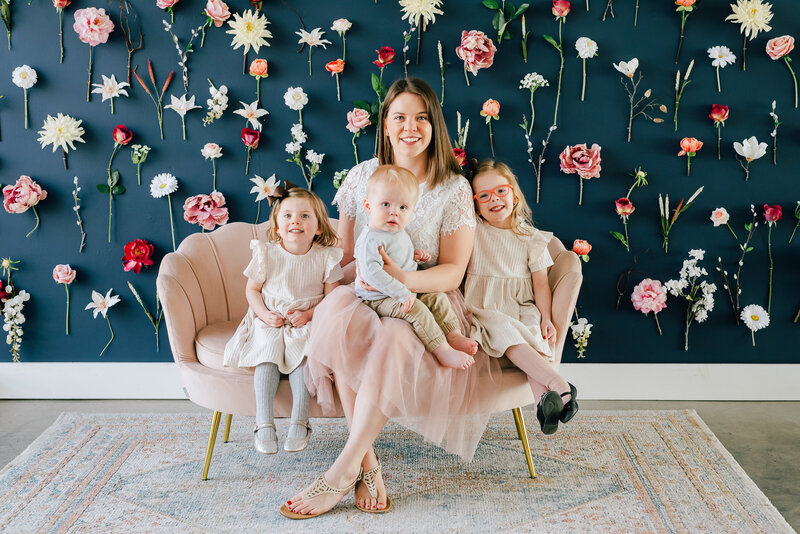 colorado wedding photographers sitting with her three children in a studio session with a floral wall behind them as they sit on a pink couch