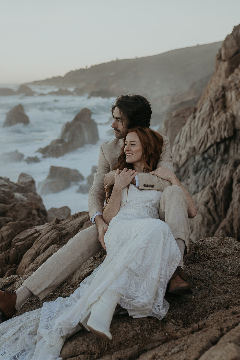 Bride and groom sitting on rock overlooking ocean during their California elopement in Big Sur