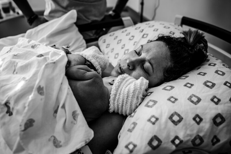 Black and white photo  of a woman lying in bed holding a newborn baby