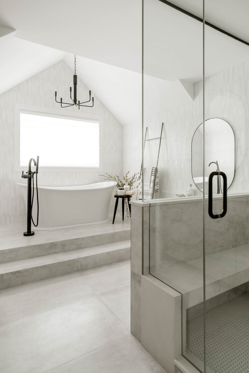 An ensuite renovation with grey and white tile and free standing tub with black accents. 