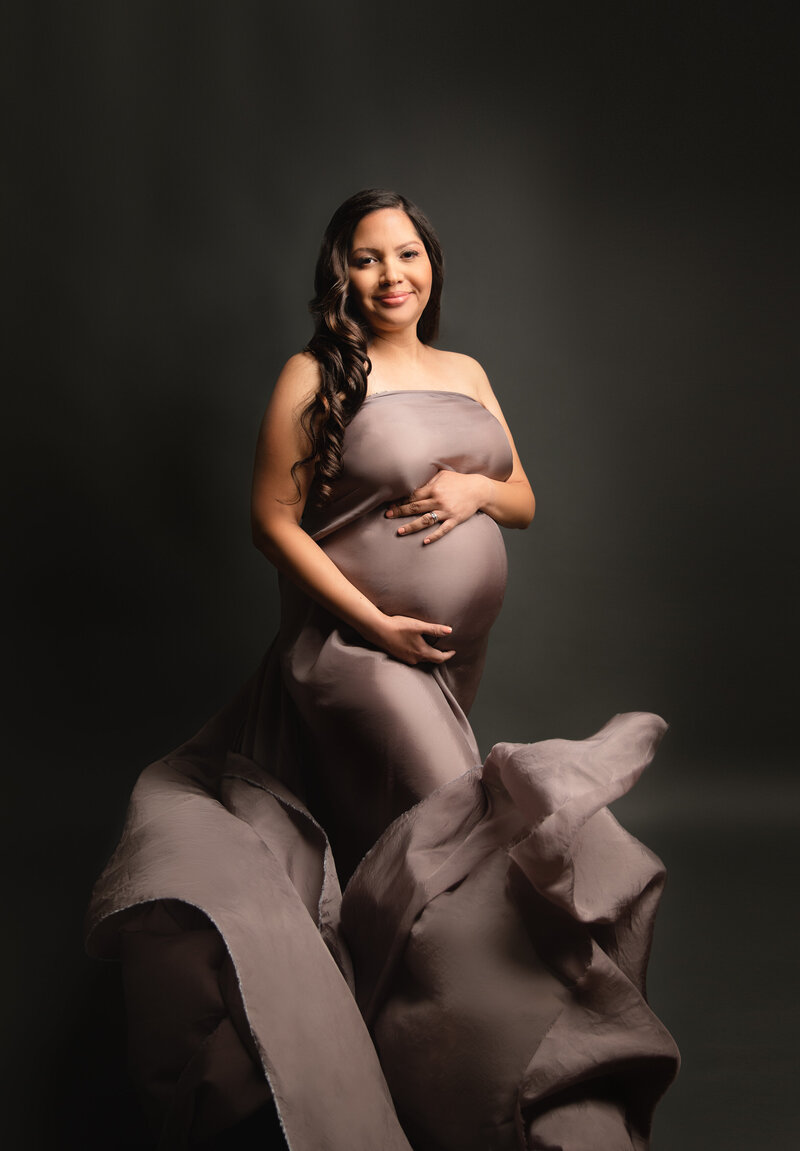 beautiful pregnant mom in the Tucson studio for her maternity session wearing gray flowing fabric