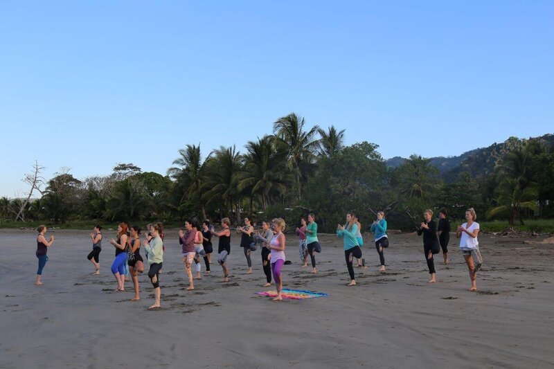 Students and teacher practicing yoga on the beach during yoga certification program in Costa Rica
