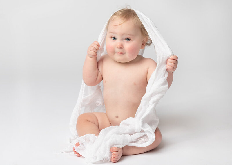 Baby on white background smiling with a blanket over his head