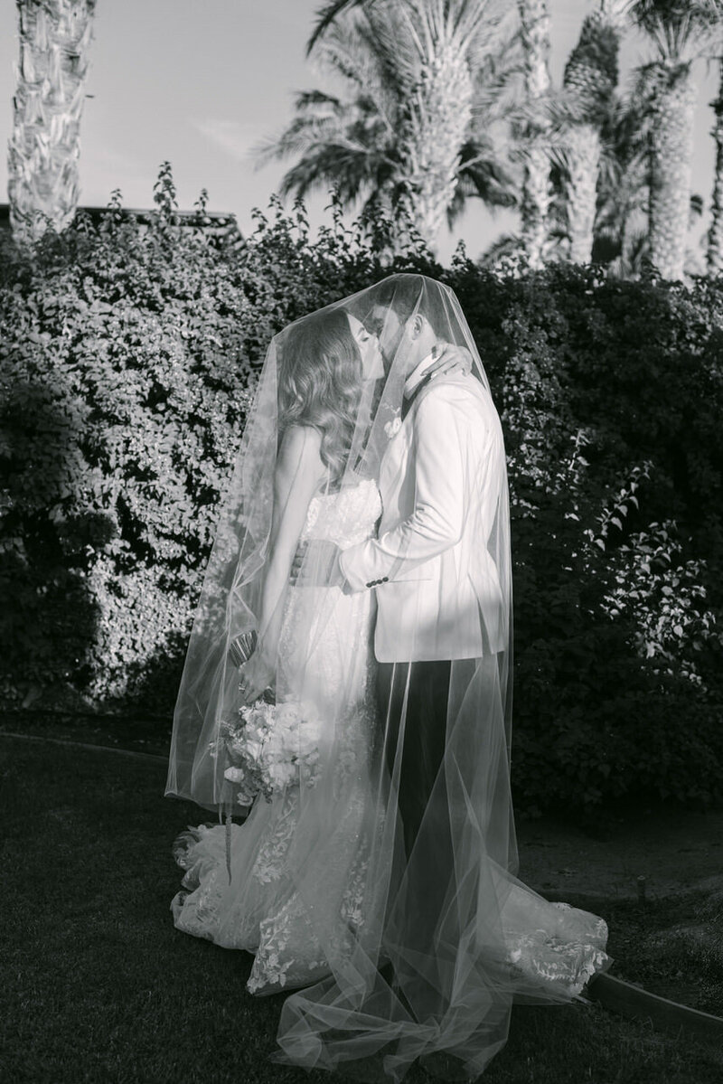 An intimate black-and-white moment of the bride and groom beneath her veil at a destination wedding in Palm Springs, CA, captured by Elizabeth Kane Photography—serving Philadelphia, New York, and DC with an artful, everlasting approach.