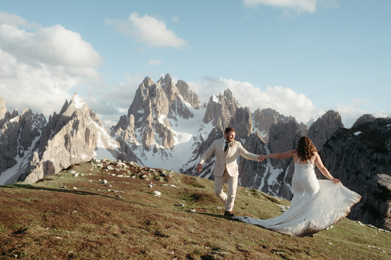 Dolomites Elopement | Bride and Groom hold hands and dance with mountains in the background