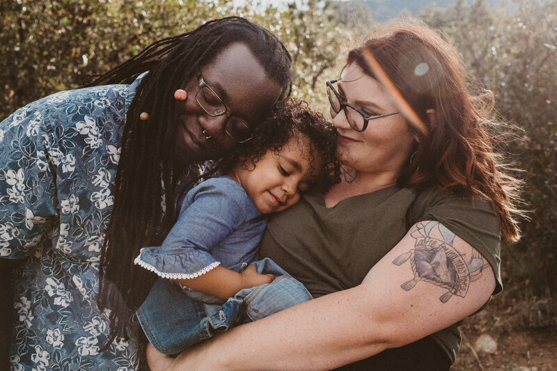 biracial family with daughter outdoors in colorado hugging and snuggling with the sunshine backlighting their hair
