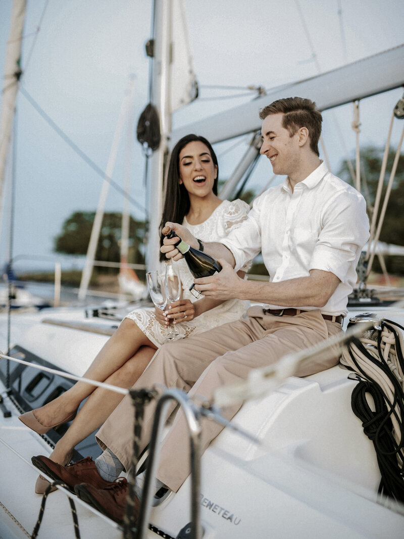 engaged-couple-celebrating-popping-champagne-on-sailboat