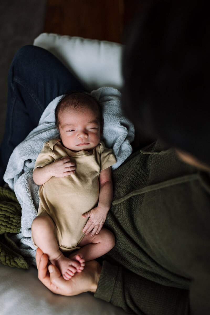 birds-eye view of newborn on a blanket in Dad's lap with one eye open during Bay Area photography session