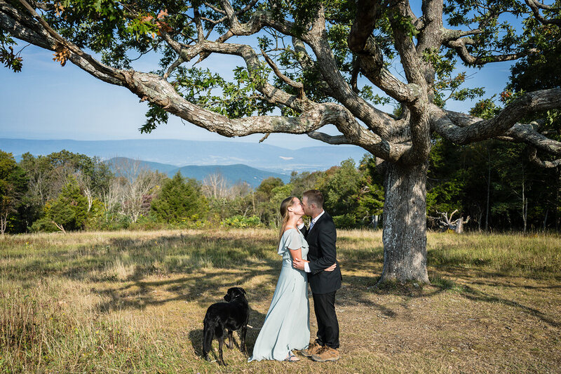 A couple goes in for a kiss during their elopement wedding day ceremony with their dog by their side at Shenandoah National Park.