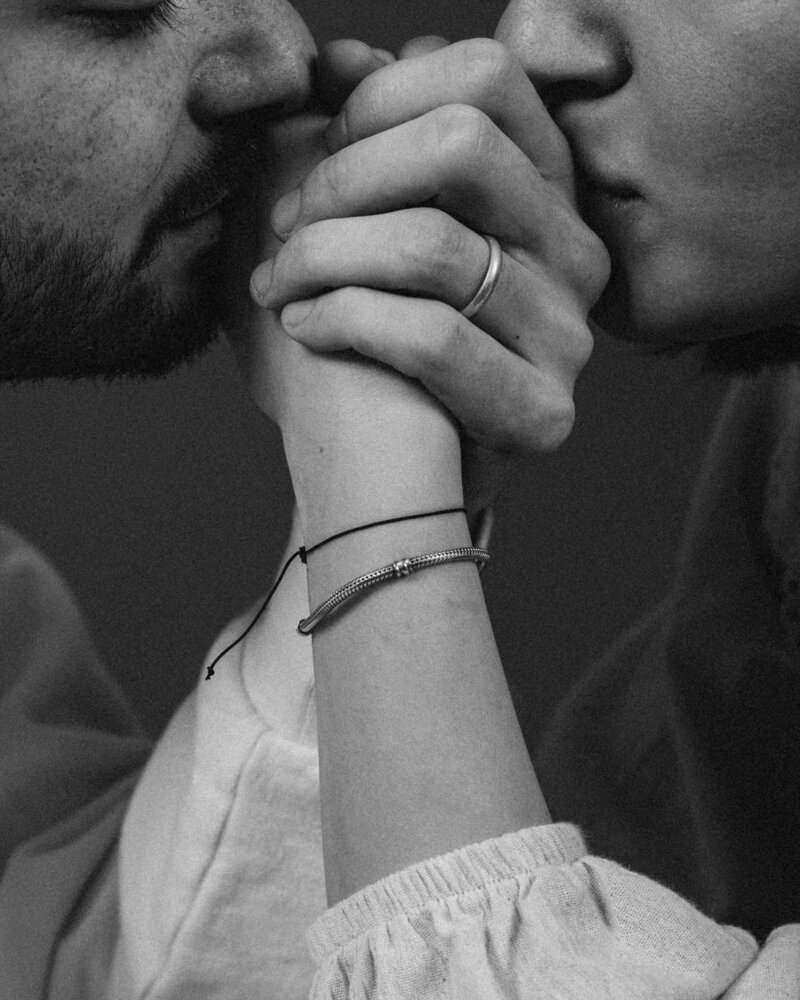 Black and white photo of a couple intimately kissing each others hands