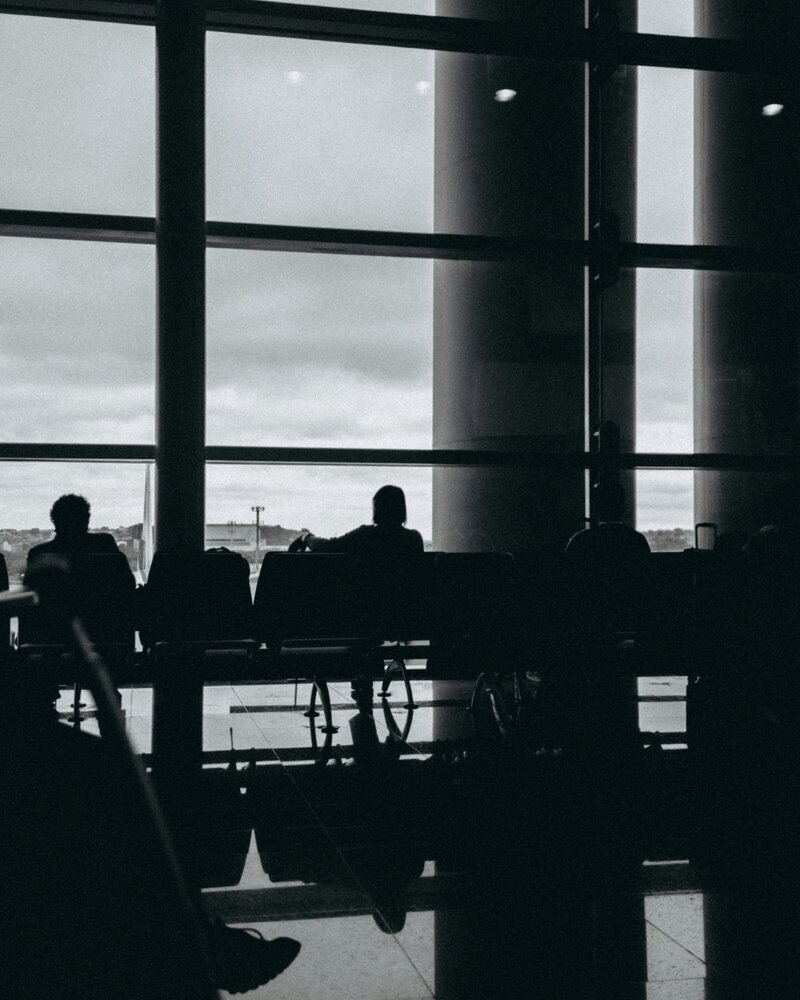 Black and white image of people sitting in seats in front of airport windows