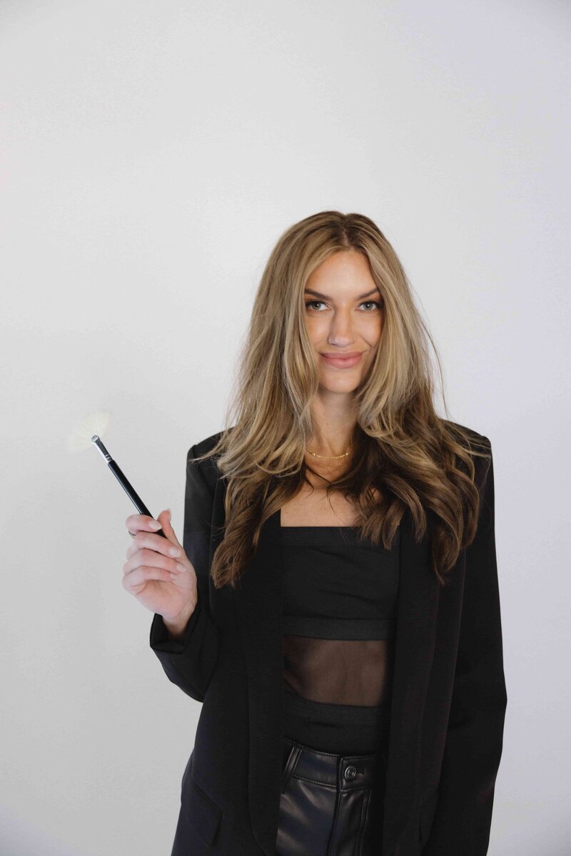 A person receiving a luxurious facial treatment is lying down with eyes closed. An esthetician, in a white lab coat and gloves, gently applies a rejuvenating serum using a dropper and brush. A soft white towel covers the relaxed client, enhancing the serene atmosphere.