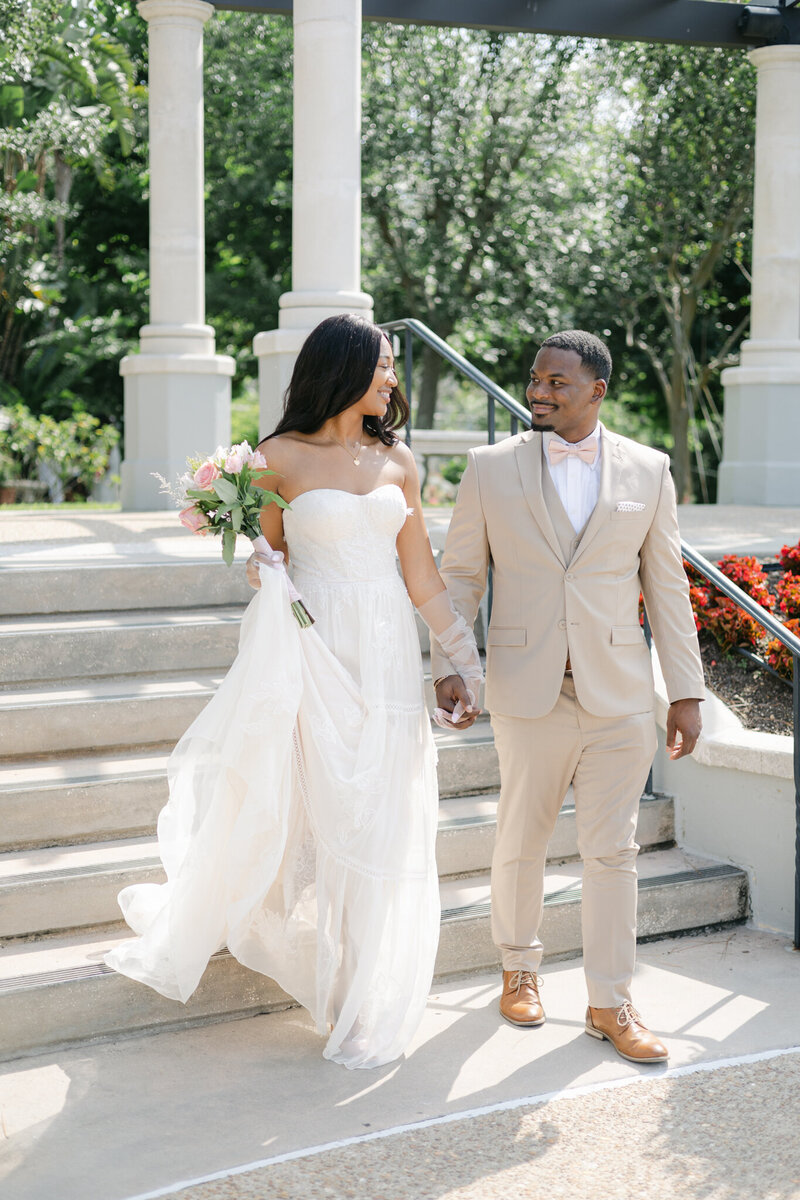Black bride and groom walk hand in hand on their wedding day through the gardens. Image captured by Sarasota wedding photographer Popping Champaign Photography